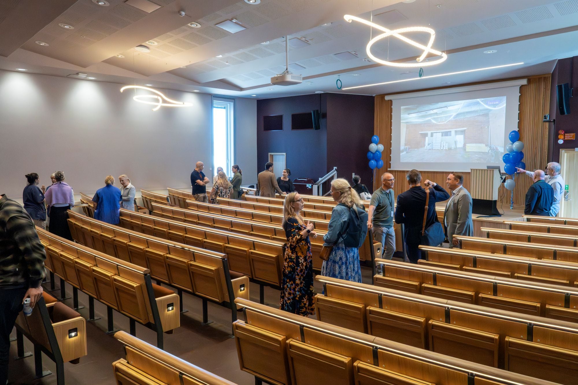 En bild &ouml;ver personer som st&aring;r och pratar i klungor i aulan d&auml;r invigningen h&ouml;lls.