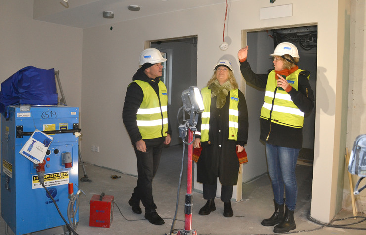 Tre personer i reflexvästar och hjälm står på en byggarbetsplats.
