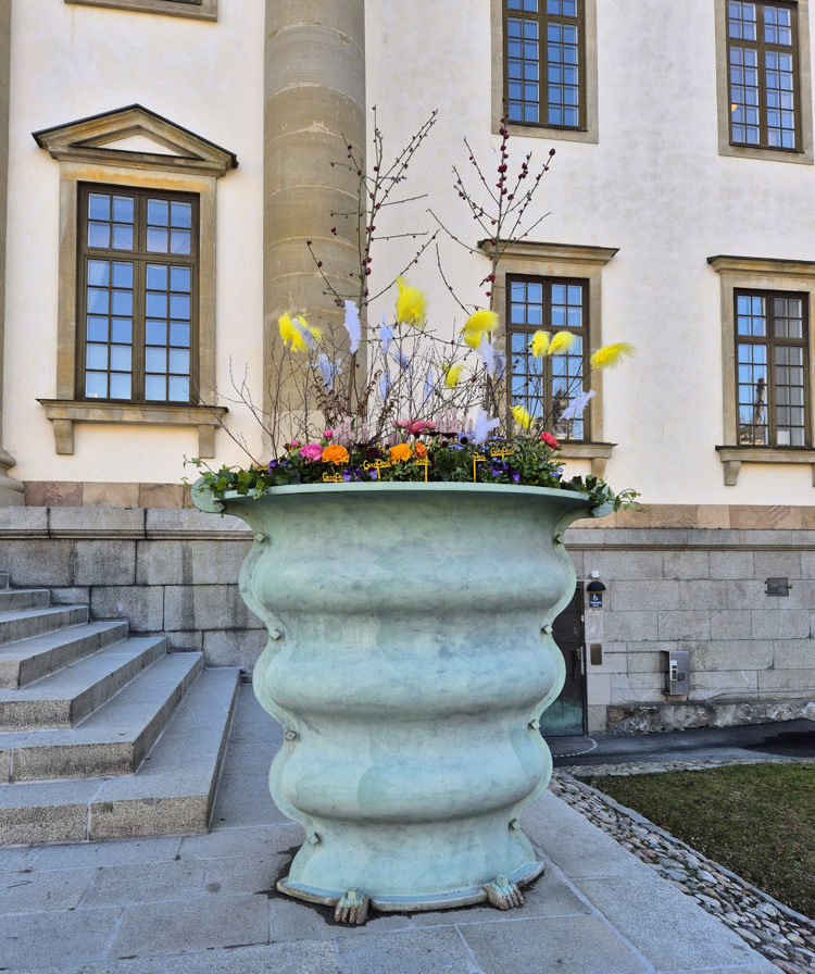 Stor kruka med f&auml;rgglada blommor och fj&auml;drar med flera glad p&aring;sk-skyltar.