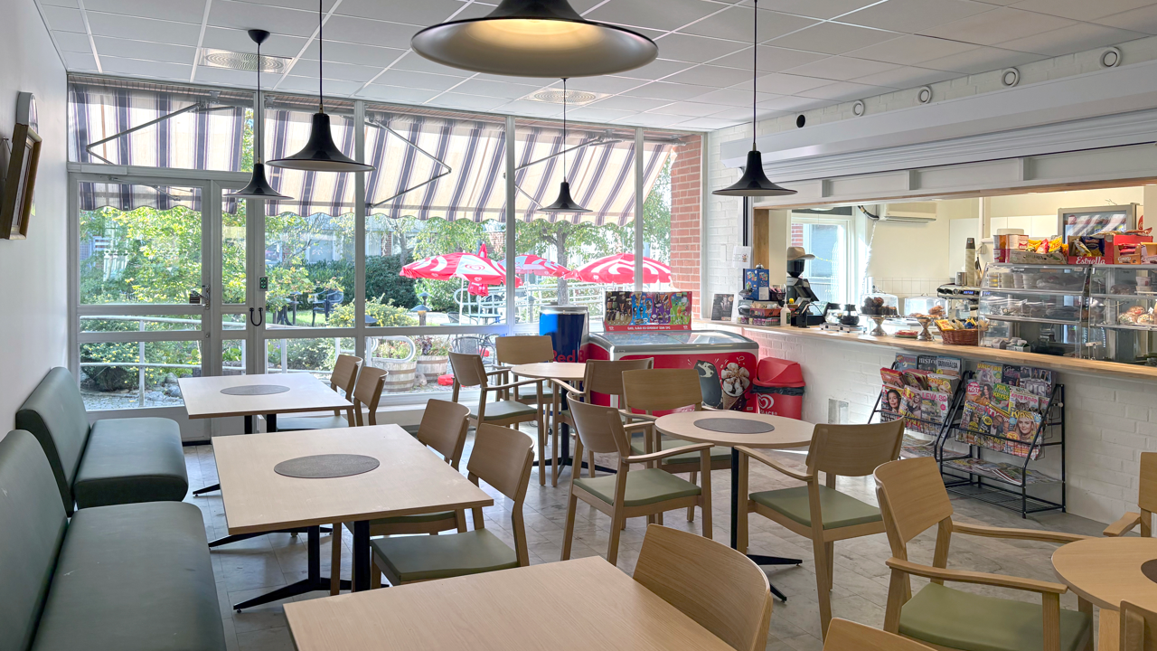 Café med bord, stolar och en disk. Stora fönster mot innergården.