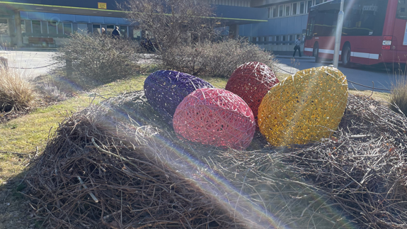 Stort fågelbo på gräsmatta med färgglada påskägg utanför sjukhusentrén.