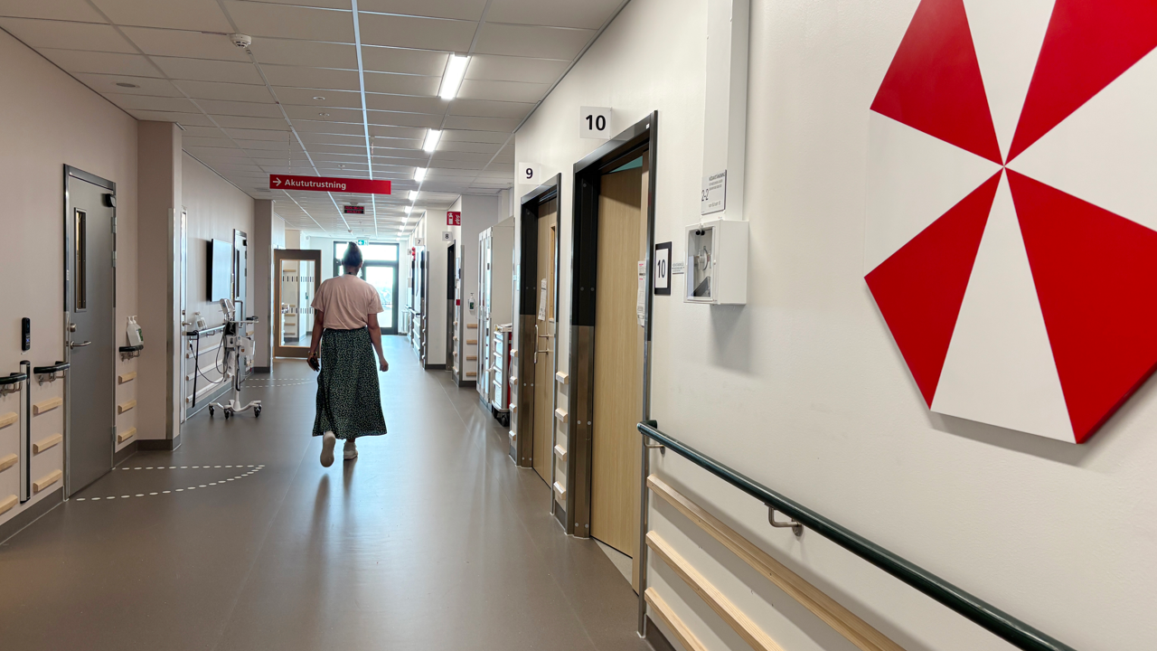 Kvinna g&aring;r i v&aring;rdkorridor med vitr&ouml;d konst p&aring; v&auml;gg.