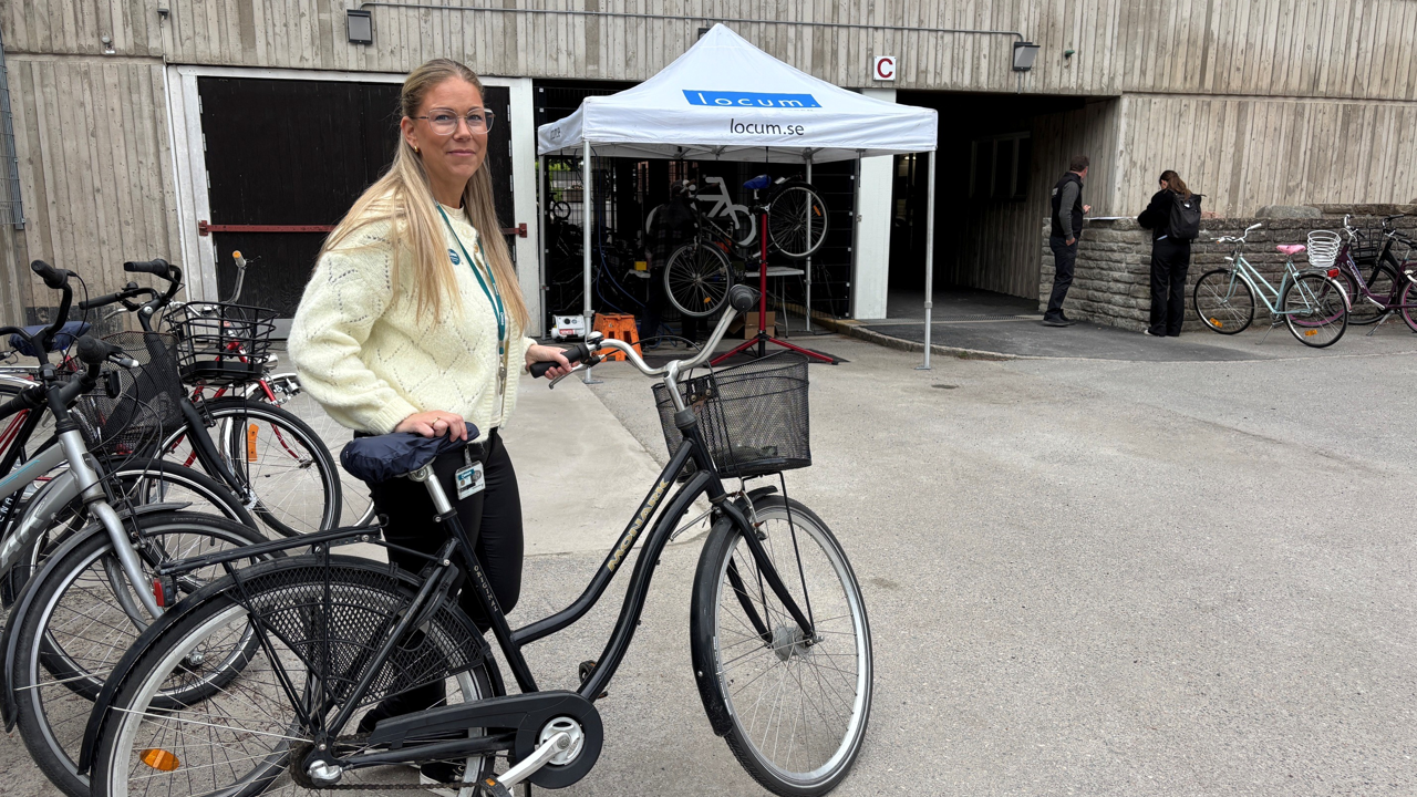 Kvinna i vit skjorta står vid svart cykel.
