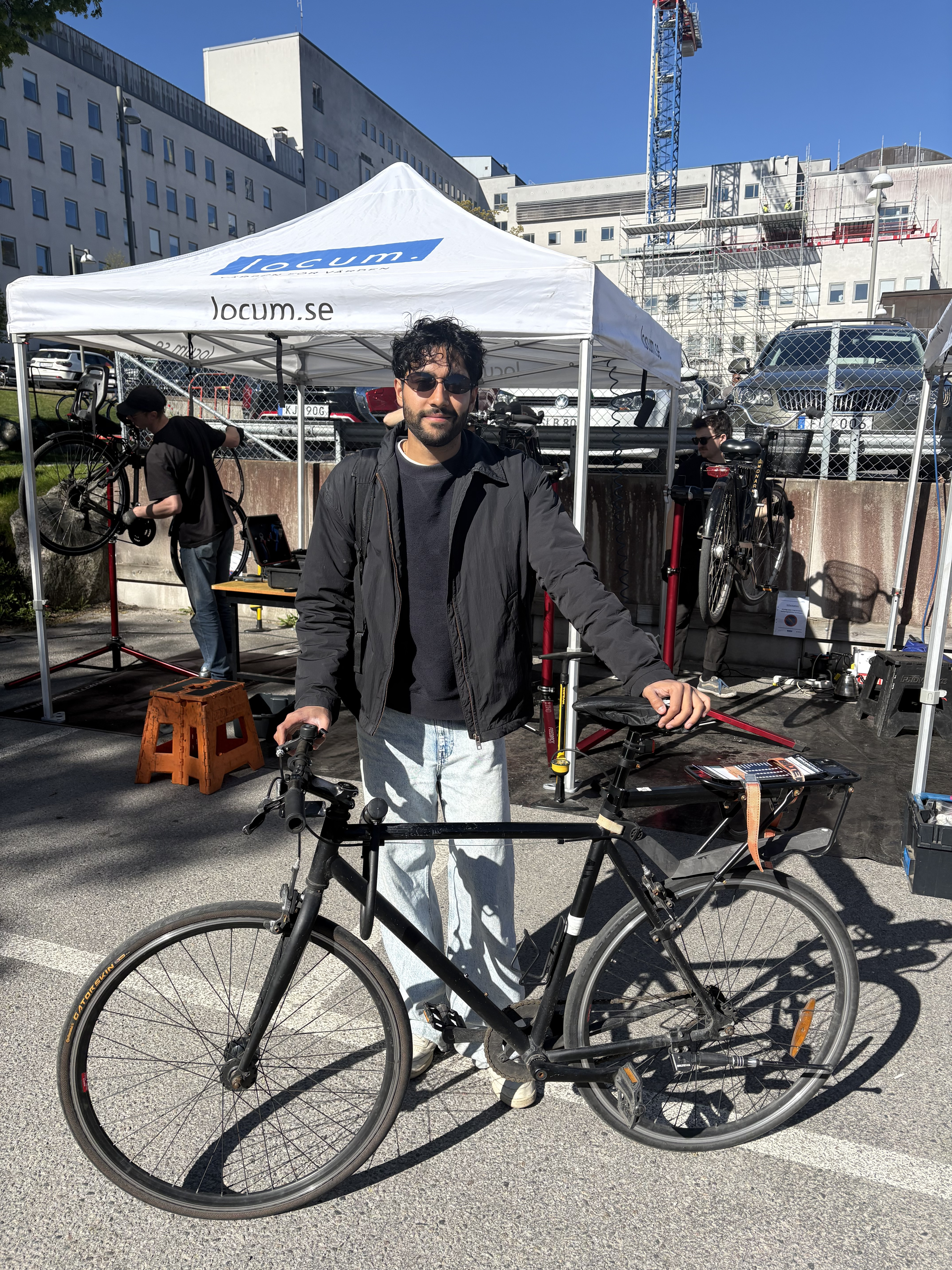 En man står med solglasögon och sin cykel framför ett av tälten för cykelservice.