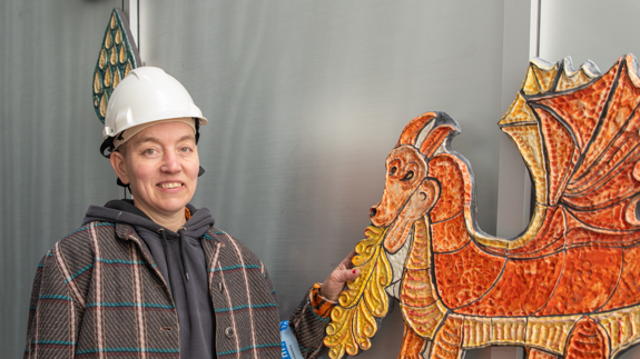 En kvinna i skyddshjälm står bredvid ett konstverk i keramik. 