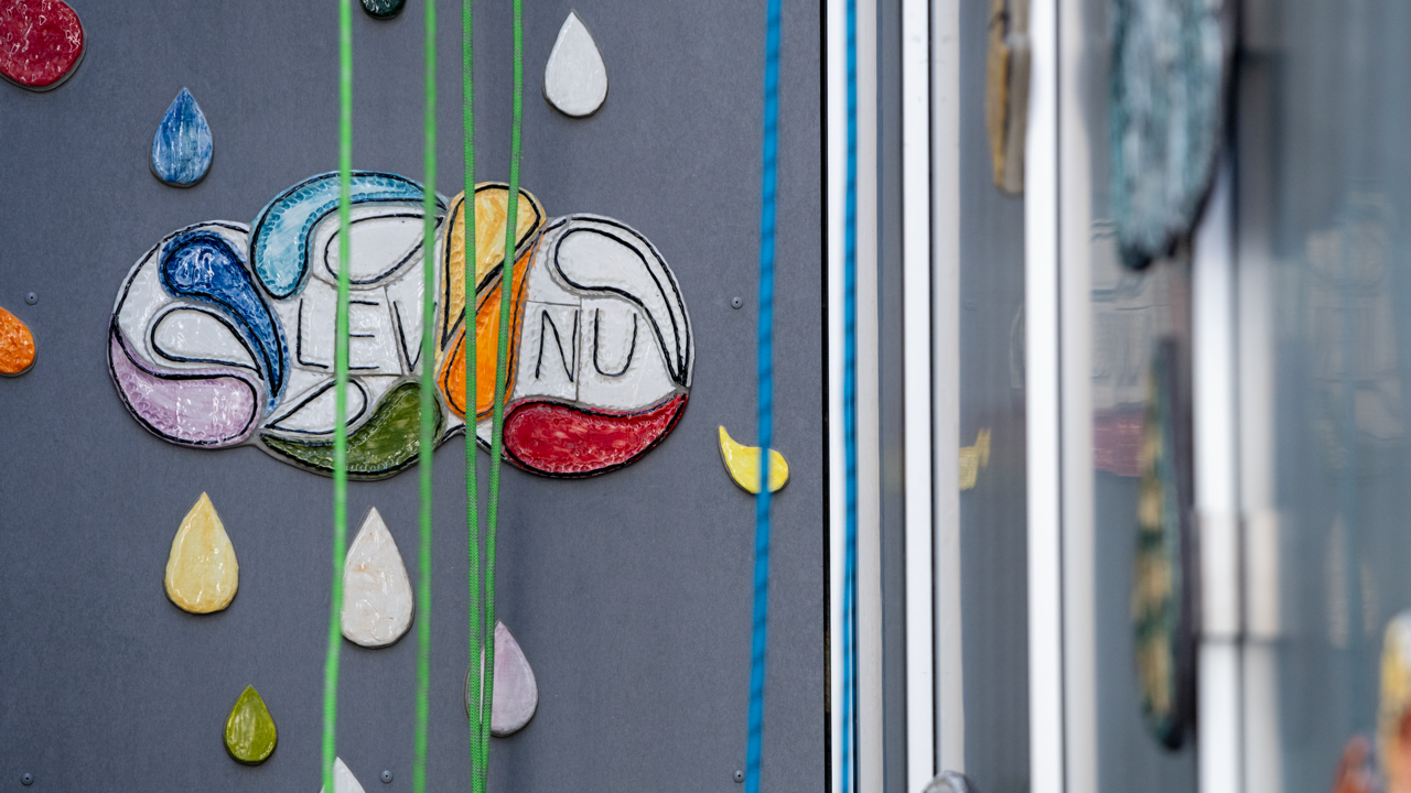 En n&auml;rbild av en skylt p&aring; en v&auml;gg. Lev nu.