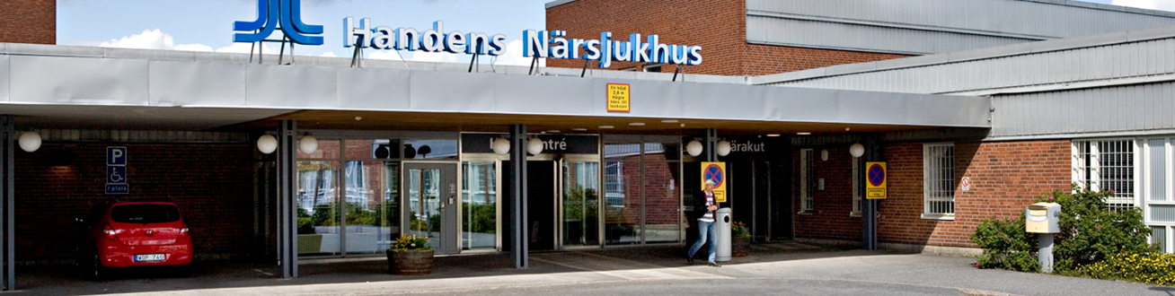 Entré till Handens sjukhus, tegelbyggnad, lövträd, gräsmatta, två bilar står parkerade bredvid entrén.