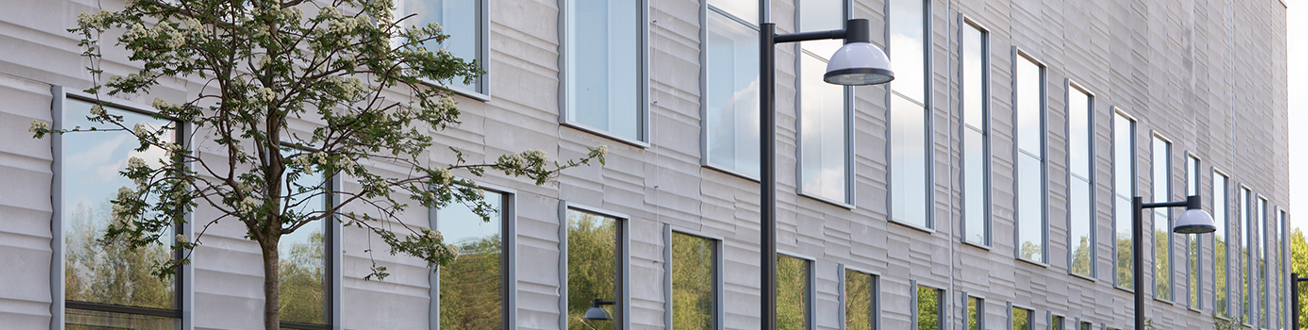 Grå fasad på operationsbyggnad som omges av grönskande träd.