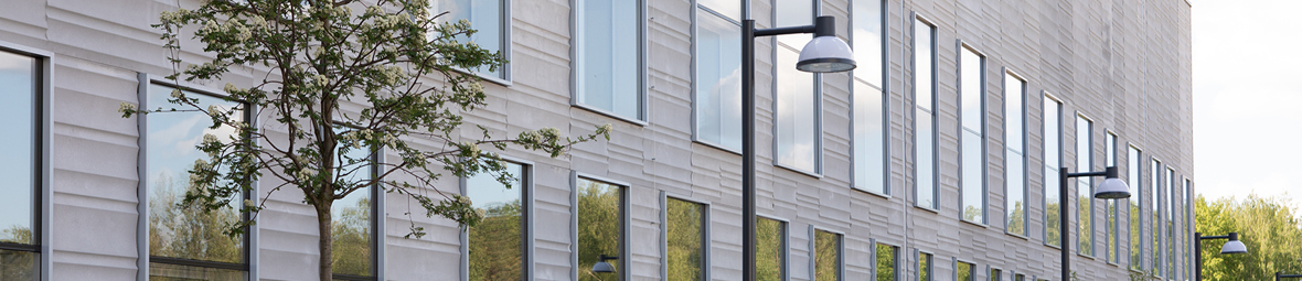 Grå fasad på operationsbyggnad som omges av grönskande träd.