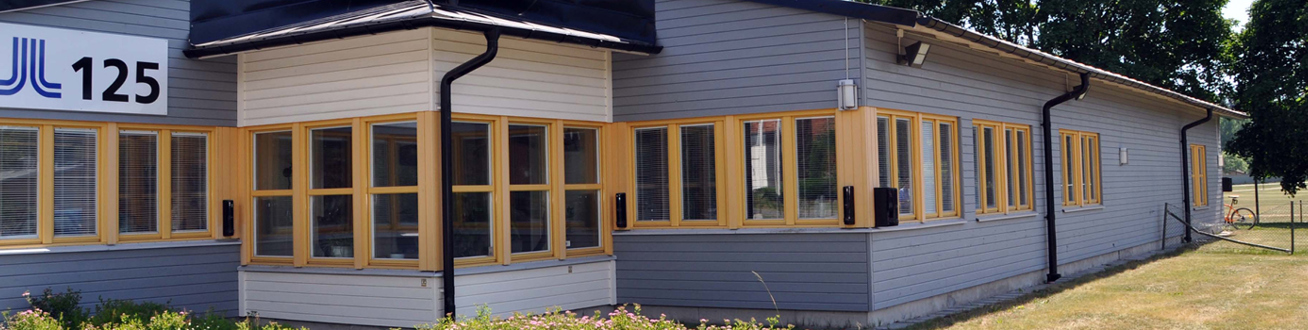 Solig blåvit fasadbild över Lindegården, röd bil står parkerad.