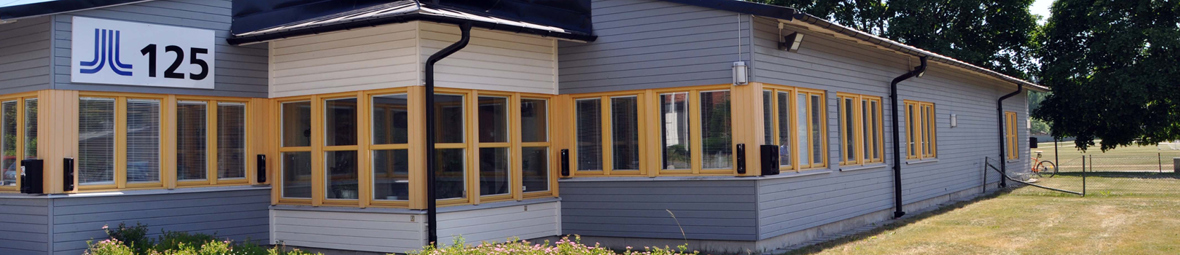 Solig blåvit fasadbild över Lindegården, röd bil står parkerad.