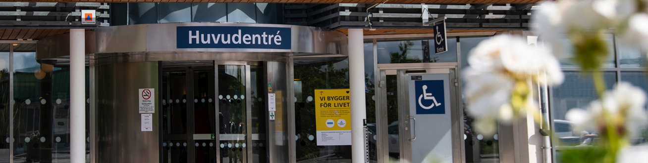 Nacka sjukhus entré med svängdörr och blommor i förgrunden.