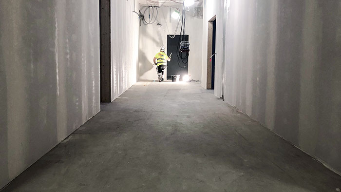 En lång korridor i betong där en byggarbetare står och målar.