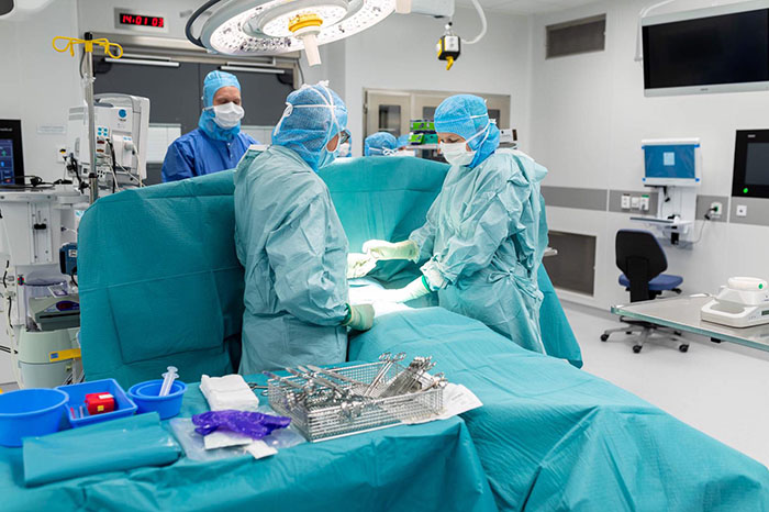 En operation med en patient på britsen.Tre personal klädda i operationskläder finns runt britsen.