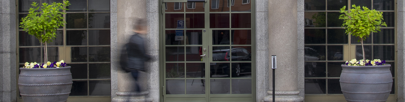 Entré till Bröstcentrum inrammad av två krukor med växter i.  En  "suddig" person är på väg mot entrén.