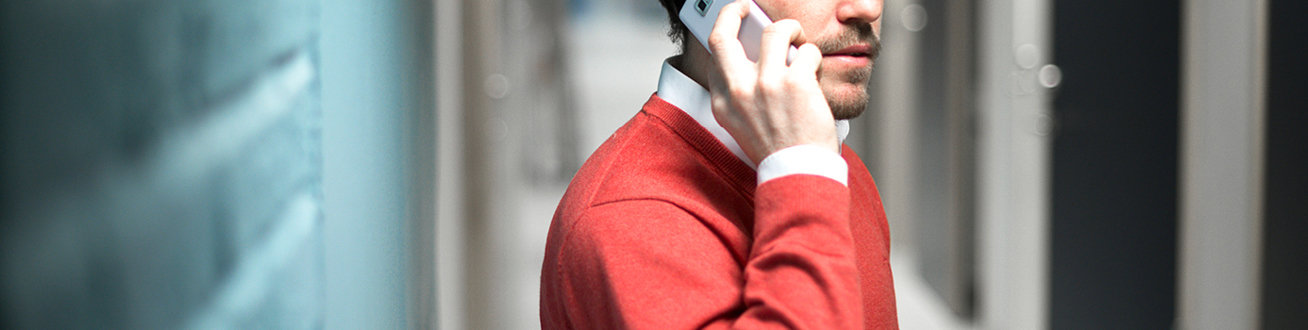 Man i röd tröja som pratar i telefon framför en blå tegelvägg.