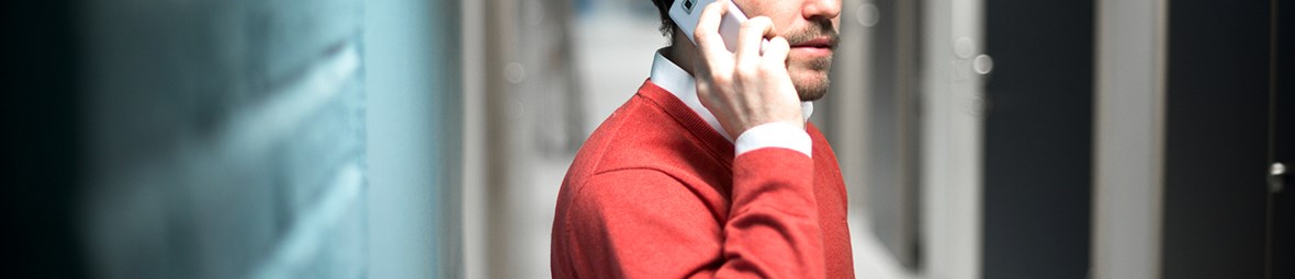 Man i röd tröja som pratar i telefon framför en blå tegelvägg.