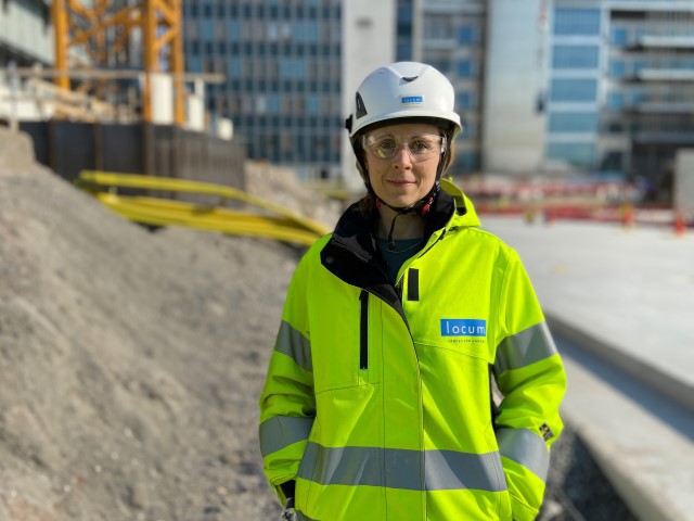 En kvinna i bygghjälm och varseljacka på en byggarbetsplats. 