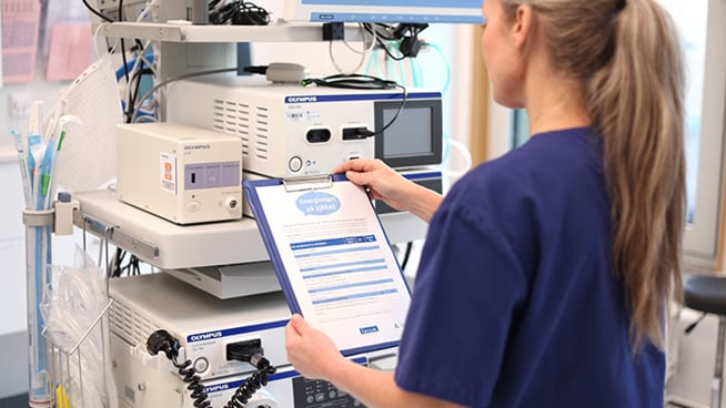 Ryggtavlan på en kvinna i vårdkläder som står framför en apparat.