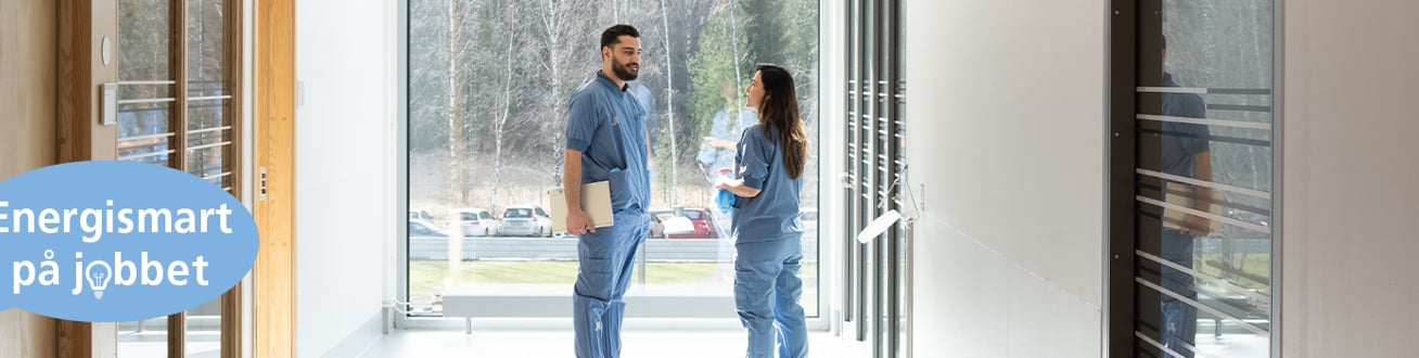 Vårdpersonal som står framför ett stort fönster i en korridor.