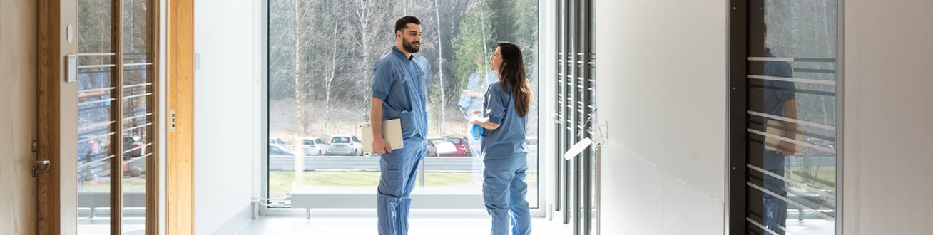 Vårdpersonal som står framför ett stort fönster i en korridor.