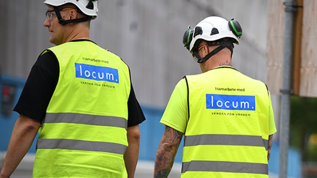 Två byggarbetare med varselväst går från kameran