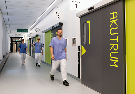 Tre personer i vårdkläder går i sjukhuskorridor