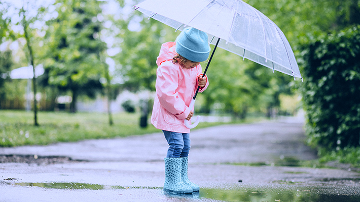 Flicka i regnjacka med paraply.