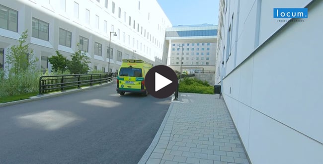 Ambulans som kar på väg mellan vita byggnader.