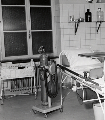 Historiskt svartvitt foto av ett vårdrum med en behållare för medicinsk gas.