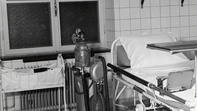 Historiskt svartvitt foto av ett vårdrum med en behållare för medicinsk gas.