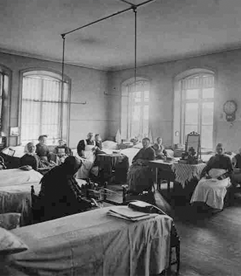 Historiskt svartvitt foto av patienter och vårdpersonal i en stor vårdsal.