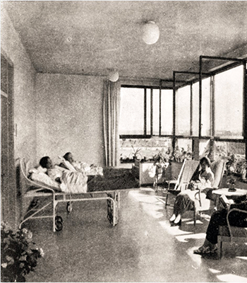 Historiskt svartvitt foto av ett antal patienter  liggandes i sängar på en inglasad balkong.