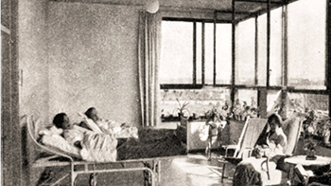 Historiskt svartvitt foto av ett antal patienter  liggandes i sängar på en inglasad balkong.