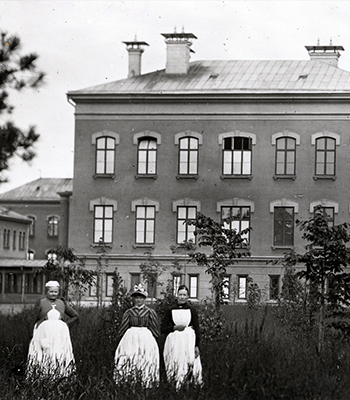 Historiskt svartvitt foto av centralbyggnaden vid S:t Görans sjukhus och tre vårdklädda kvinnor. 