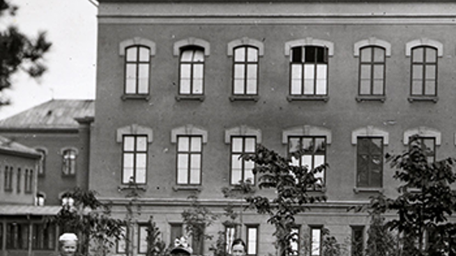 Historiskt svartvitt foto av centralbyggnaden vid S:t Görans sjukhus och tre vårdklädda kvinnor. 