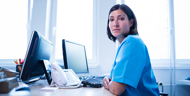 Kvinna i blå skjorta sitter framför en dator.