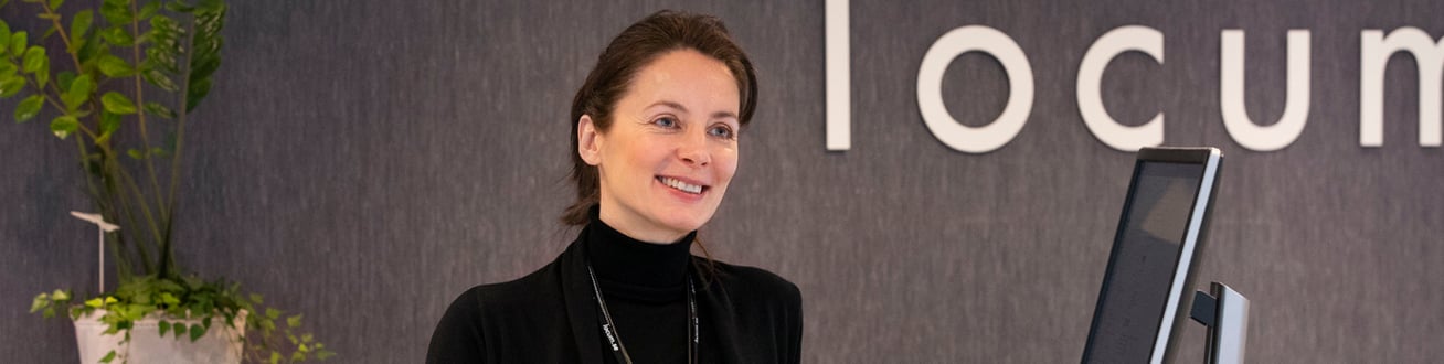 Grön växt till vänster, Locums kvinnliga recepetionist ler välkomnande. Stor locum logotyp syns till höger.